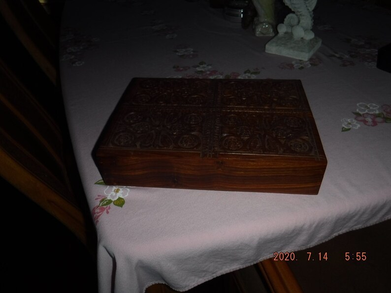 May include: A dark brown wooden box with intricate carvings on the top and sides. The box has a hinged lid and is closed.