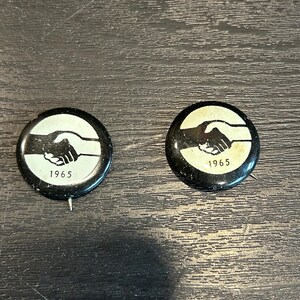 May include: Two black and white round buttons with a handshake design and the year 1965 printed on them.
