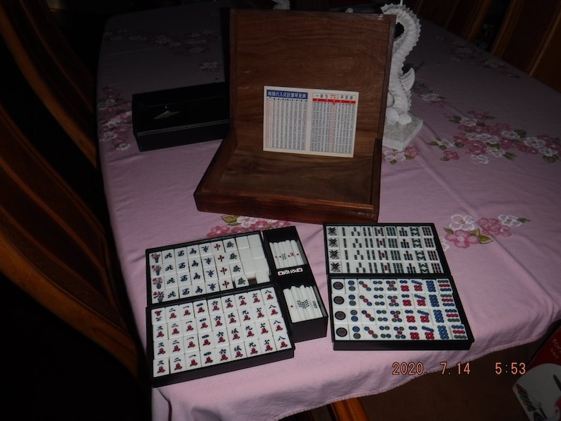 May include: A wooden box with a set of mahjong tiles. The tiles are arranged in two rows, with the top row showing the numbers 1 through 9 and the bottom row showing the characters for wind, dragon, and flower. The box is open and the tiles are visible.