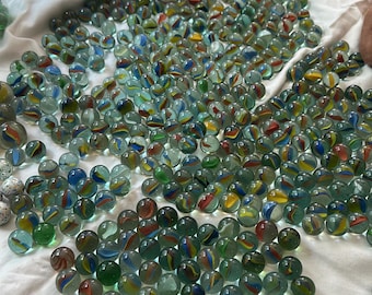 May include: A large collection of colorful glass marbles with swirling patterns of red, yellow, blue, and green. The marbles are scattered on a white cloth, creating a vibrant display of classic toys.