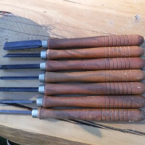 May include: A set of seven wood carving tools with wooden handles. The tools have different blade shapes and sizes.