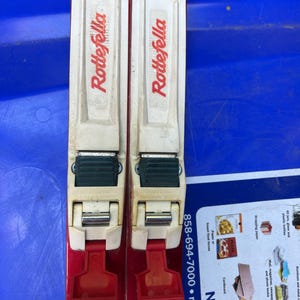 May include: A pair of red ski poles with white and green bindings. The poles have the word "Dragopod" printed on them in red letters.