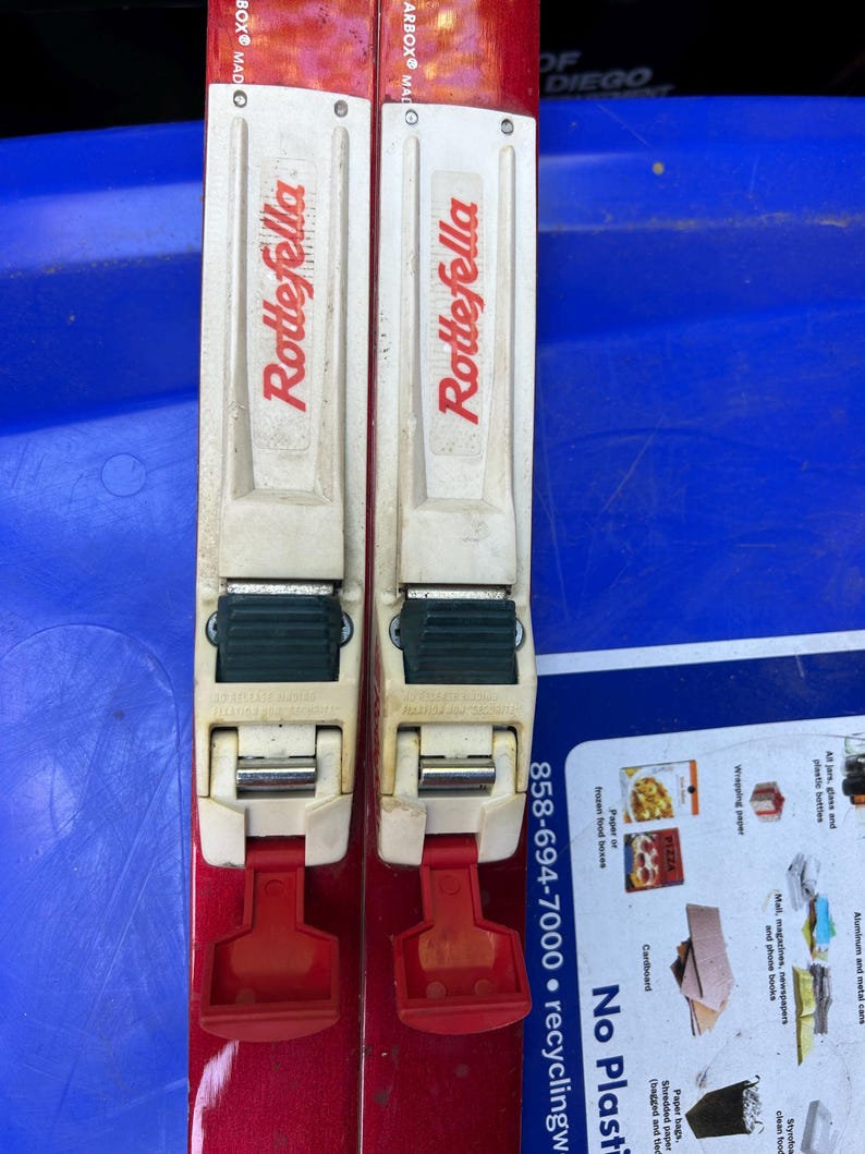 May include: A pair of red ski poles with white and green bindings. The poles have the word "Dragopod" printed on them in red letters.