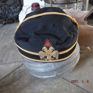 May include: A black Masonic hat with gold trim and a gold embroidered emblem featuring a red triangle and two eagles.