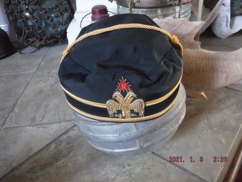 May include: A black Masonic hat with gold trim and a gold embroidered emblem featuring a red triangle and two eagles.