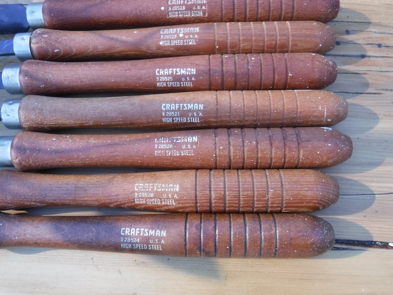 May include: A set of eight wood-handled chisels with silver blades. Each chisel has a white label with the text "CRAFTSMAN" and "HIGH SPEED STEEL".