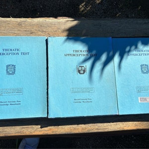 May include: Three blue books with the title "Thematic Apperception Test" printed on the front. The books are from Harvard University Press, Cambridge, Massachusetts.