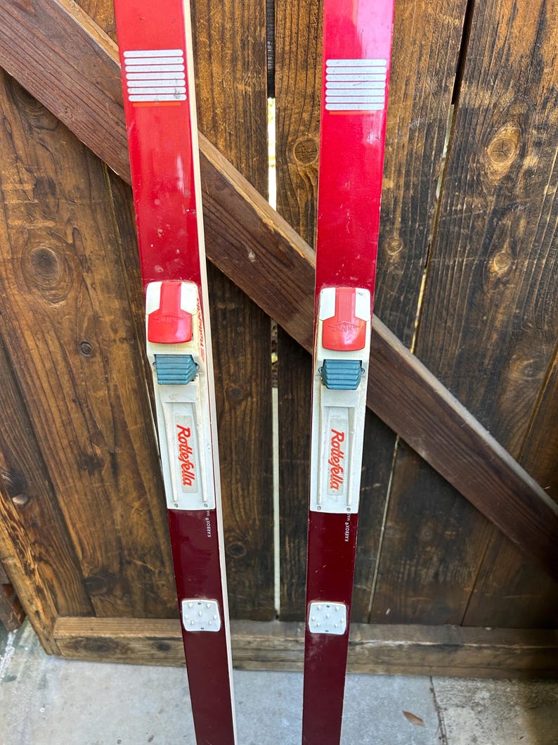 May include: A pair of red vintage cross-country skis with white bindings and the text "Rollefella" printed on the side.