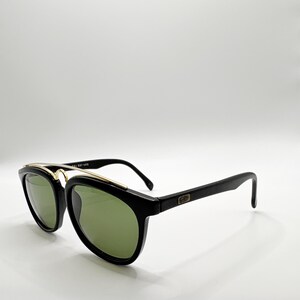 May include: Black sunglasses with green lenses and gold accents. The sunglasses have a classic design with a thick black frame and a gold bridge. The lenses are a dark green color, and the arms are black. The sunglasses are a stylish accessory.