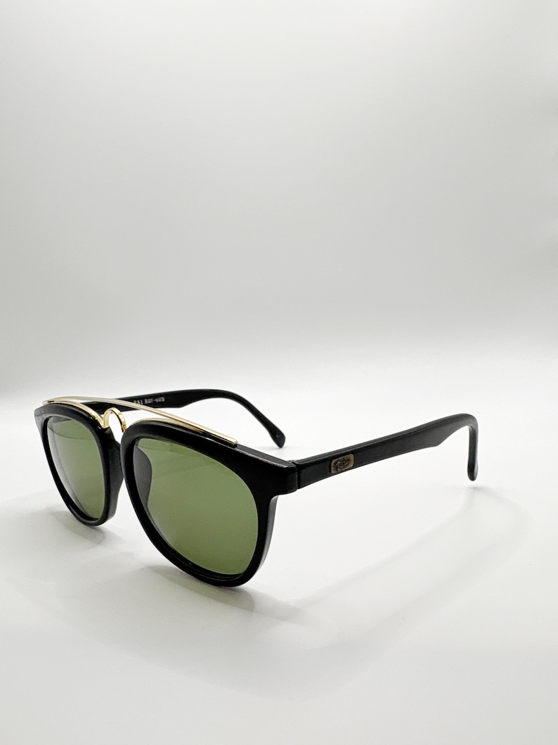 May include: Black sunglasses with green lenses and gold accents. The sunglasses have a classic design with a thick black frame and a gold bridge. The lenses are a dark green color, and the arms are black. The sunglasses are a stylish accessory.