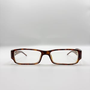 May include: Rectangular eyeglasses with a tortoiseshell pattern. The frames are a mix of brown and amber hues, with clear lenses. The glasses have a classic, understated design.
