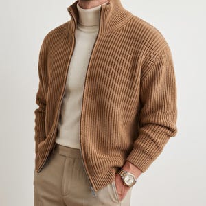 Può includere: Un cardigan con zip in maglia a coste color marrone chiaro indossato sopra un maglione a collo alto color crema e pantaloni color kaki chiaro. Il cardigan presenta un collo alto e una cerniera in metallo argentato. È visibile un orologio argentato.