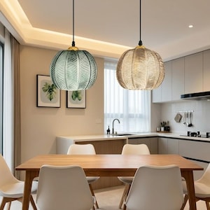 Peut inclure: Deux lampes suspendues avec des abat-jours en verre texturé sont suspendues au-dessus d'une table à manger en bois. Un abat-jour est vert, l'autre est beige. Les lampes ont des accents dorés et sont suspendues à des cordons noirs.