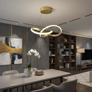 Peut inclure: Un luminaire suspendu moderne de couleur dorée avec un design à double boucle, émettant une douce lueur chaude. Le luminaire est suspendu au-dessus d'une table à manger, complétant le décor contemporain de la pièce. La pièce présente un schéma de couleurs gris.