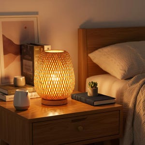 Peut inclure: Une lampe de chevet chaleureuse avec un abat-jour ajouré tissé, créant une ambiance douce. La lampe est posée sur une table de chevet en bois, à côté d'une petite plante succulente en pot et d'un livre.