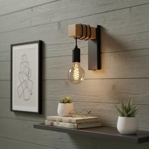 Peut inclure: Une applique murale moderne avec une base en métal noir et un élément en bois. L'applique est équipée d'une grande ampoule Edison ronde. Le luminaire est fixé sur un mur en bois gris. Une œuvre d'art abstraite encadrée et une étagère avec des livres et des plantes sont également visibles.