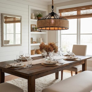 Puede incluir: Un comedor con una gran mesa de madera oscura preparada para una comida. Una lámpara de araña de cuerda trenzada y metal cuelga por encima. La habitación incluye un espejo, estanterías y una ventana con una persiana de bambú. La mesa está puesta con platos, vasos y cubiertos.