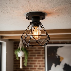 Könnte beinhalten: Schwarze geometrische Deckenleuchte mit sichtbarer Edison-Glühbirne. Die Leuchte ist an einer weißen Decke montiert. Die Leuchte hat ein modernes, industrielles Design, das für Wohn- oder Gewerberäume geeignet ist.
