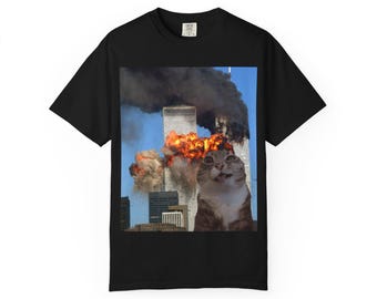 May include: Black t-shirt featuring a meme of a cat with wide eyes in front of the burning Twin Towers. The image is set against a blue sky with smoke and flames. The cat is brown and white.