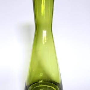 May include: A tall, green glass vase with a flared base and a slender, hourglass-shaped body. The vase has a wide opening at the top and is made of transparent glass. The vase is approximately 30 cm tall.