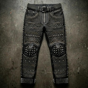 Könnte beinhalten: Schwarze Lederhose, stark mit silbernen Spikes und Nieten besetzt. Die Hose hat einen Reißverschluss, Gürtelschlaufen und einen Nietengürtel. Größere Spikegruppen zieren die Knie und Unterschenkel, was einen kühnen Look erzeugt.