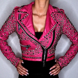 May include: A hot pink leather jacket with silver-toned studs and zippers. The jacket has a classic biker style with a notched collar, asymmetrical zipper closure, and zippered pockets. The sleeves and shoulders are heavily embellished with studs.
