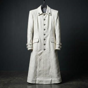May include: A long, white coat with a textured, snake-like pattern. The coat features a button-down front, two pockets, and decorative buckles on the sleeves. The coat is hanging on a black hanger against a dark background.