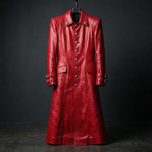Könnte beinhalten: Ein langer, roter Ledermantel mit strukturierter Schlangenmusterung. Der Mantel hat eine Knopfleiste, zwei Taschen und dekorative Knöpfe an den Manschetten. Er hängt an einem schwarzen Kleiderbügel vor dunklem Hintergrund.