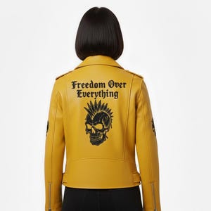 Puede incluir: Chaqueta motera amarilla mostaza con un gráfico de calavera negra y el texto "Freedom Over Everything" en la espalda. La chaqueta tiene un cierre de cremallera asimétrico clásico, charreteras y mangas con cremallera. Una pieza audaz.