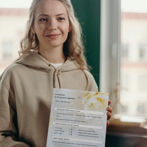 Peut inclure: Une personne tient un agenda imprimé intitulé « Agenda émotionnel et productif ». L'agenda comprend des sections pour un bilan émotionnel matinal, des objectifs basés sur l'humeur, une pause émotionnelle et une réflexion du soir. L'agenda a un design floral.