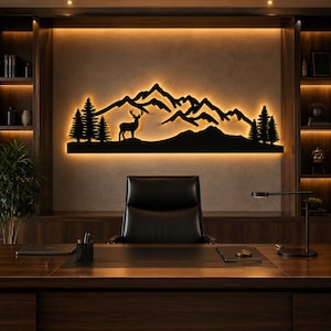 May include: A black metal wall art piece featuring a silhouette of a deer standing in front of a mountain range with pine trees on both sides. The artwork is backlit with warm light, creating a glowing outline against the wall surface.