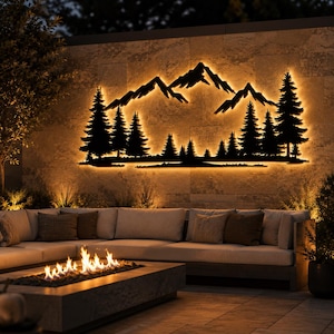 May include: A black metal wall art piece featuring a silhouette of a mountain range and a dense forest of pine trees. The design is backlit with warm LED lighting, creating a glowing outline that highlights the jagged peaks and tree shapes.