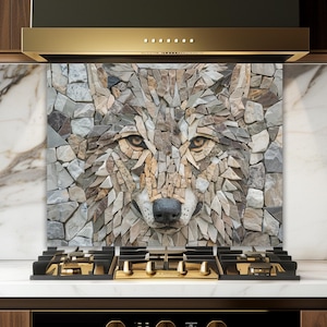 Puede incluir: Un protector contra salpicaduras de cocina con un rostro de lobo en mosaico, hecho de piedras grises, marrones y beige. La obra de arte está instalada sobre una encimera negra con detalles dorados, frente a gabinetes de madera.