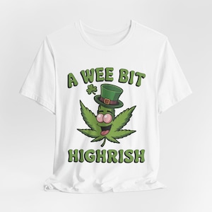 Könnte beinhalten: Weißes T-Shirt mit einer grünen Cannabisblatt-Figur, die einen grünen Zylinder trägt. Der Text "A Wee Bit Highrish" ist in Grün über und unter der Figur gedruckt, mit einem grünen Kleeblatt.