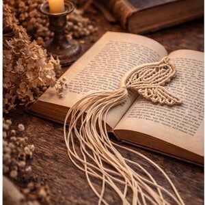 May include: An open book with aged pages, featuring a handmade macrame bookmark in a bird shape. A lit candle in a vintage holder and dried flowers sit nearby. The scene is set on a dark wooden surface, creating a cozy, vintage aesthetic.