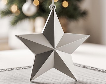 May include: A silver, five-pointed star decoration, suspended by a white string. The star is constructed from folded paper or metal, with visible seams. A Christmas tree and blurred lights are in the background.