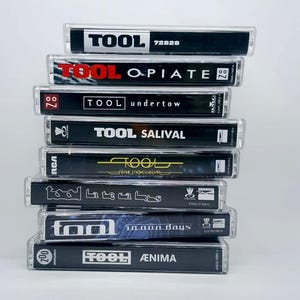 May include: A stack of Tool cassette tapes. The tapes have black and white labels with the band's name and album titles, including "Opiate," "Undertow," and "&AElig;nima." The cases are clear plastic.