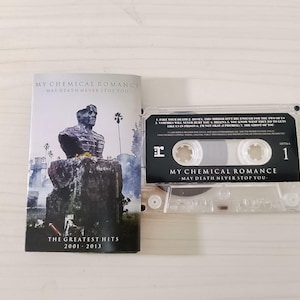 May include: A cassette tape and album cover for "My Chemical Romance: May Death Never Stop You." The album cover features a statue and the text "The Greatest Hits 2001-2013." The cassette tape is clear with black text.
