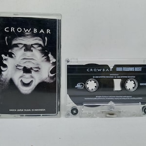 May include: A Crowbar Odd Fellows Rest cassette tape with a clear plastic case. The J-card features a black and white image of a face and the text Crowbar and Hanya Untuk Dijual Di Indonesia. The tape shell is black with white text.