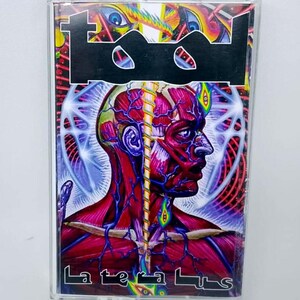May include: A cassette tape featuring the band Tool's logo in black and a vibrant, surreal illustration of a human head with exposed muscles and veins. The album title, "Lateralus," is printed in white.