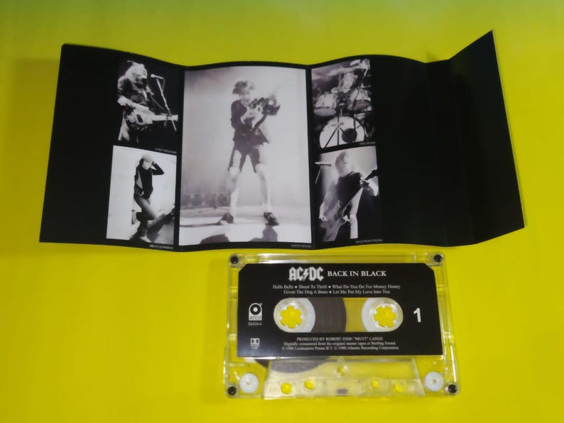May include: A cassette tape of the AC/DC album "Back in Black" with a black and white photo insert. The cassette is clear with yellow accents and the album title is printed on the label. The insert features band photos.