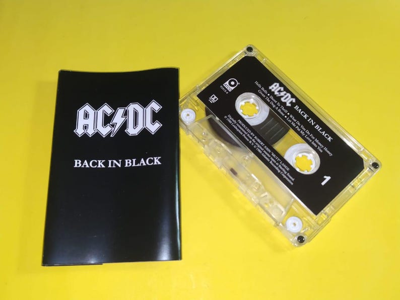 May include: A vintage AC/DC "Back in Black" cassette tape and its black case. The cassette is clear with a black label and white text. The case is black with the band's logo and album title in white.