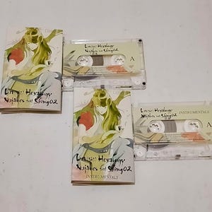 Puede incluir: Se muestran cuatro cintas de casete y sus estuches. Los estuches presentan una ilustración de una persona con pelo largo verde y detalles en rojo. El texto en los estuches y cintas dice "Luv(sic) Hexalogy Nujabes feat Shing02". Dos cintas están etiquetadas como "INSTRUMENTALS".