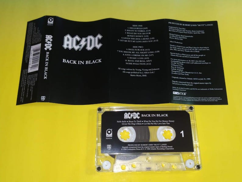 May include: AC/DC "Back in Black" cassette tape with the album cover and tracklist visible. The cassette is clear with black labels and the number 1. The album cover is black with white text.