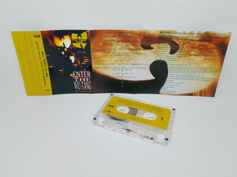 May include: A clear cassette tape with a yellow label and the text "1" is next to the open album cover of the Wu-Tang Clan's "Enter the Wu-Tang (36 Chambers)" album. The album cover is yellow and features the Wu-Tang Clan logo and album title.