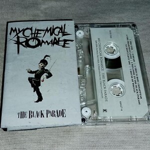 Pode incluir: É exibida uma fita cassete do álbum "The Black Parade" de My Chemical Romance. A capa do álbum apresenta o logotipo da banda e uma ilustração de um membro de uma banda marcial. A caixa da cassete é transparente.