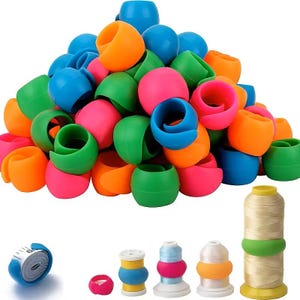 May include: A collection of colorful, C-shaped silicone thread spool huggers in bright shades of blue, orange, green, and pink. The set includes a white measuring tape secured by a blue hugger and four spools of thread wrapped with these silicone bands.
