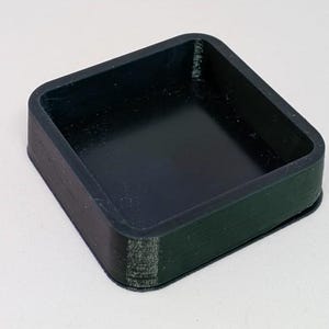 Może przedstawiać: Biały ceramiczny kubek z czarnym uchwytem i napisem "But First, Coffee" pogrubioną, czarną czcionką. Kubek jest wypełniony ciemnym płynem, prawdopodobnie kawą, i stoi na białej powierzchni.