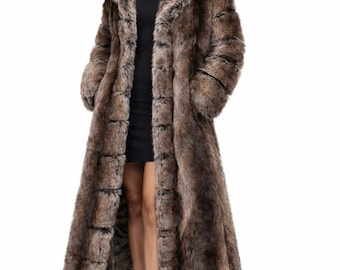 May include: A long, brown faux fur coat with a hood. The coat has a textured appearance and a dark brown and black colour scheme. The model is wearing a black dress and black boots. The coat is floor-length.