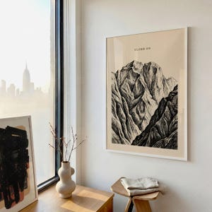 Climb On Mountain Print in frame on wall near window in minimalist office space with natural light, vintage mountain landscape poster, motivational adventure wall art with beige and black tones